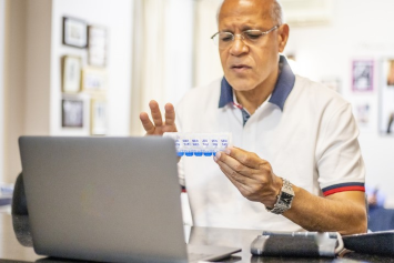 A person sitting down in front of an open laptop checks their pill organizer.